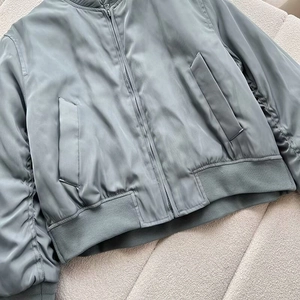 Detail view of smooth grey-green bomber jacket showing side pocket and ribbed hem texture