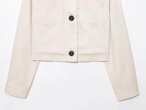 Detail of off-white cropped jacket with texture, black buttons and chest pockets