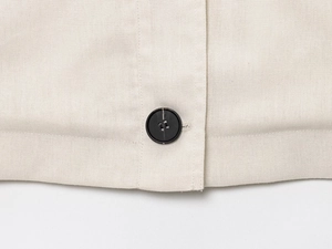 Close-up of beige linen jacket with black four-hole button and precision stitching detail