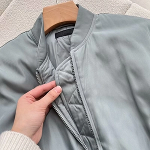 Close-up of a grey-green bomber jacket showing the metal zipper and quilted lining details