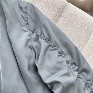 Close-up of ruched sleeve detail on a silky steel blue bomber jacket for women