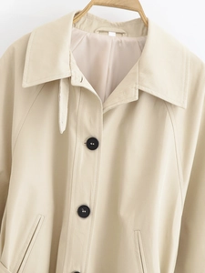 Detailed close-up of a khaki trench coat featuring wide lapels and black buttons
