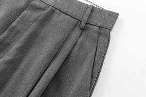 Détail du pantalon plissé gris foncé montrant la texture du sergé et les passants de ceinture