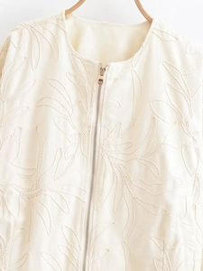 Close-up of cream textured jacket featuring intricate leaf embroidery and silver zipper detail