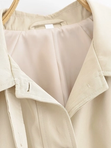 Detailed close-up of beige trench coat lapel showing twill fabric texture and stitching