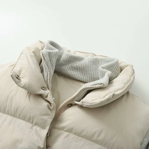 Detail of a beige jacket featuring a grey ribbed stand collar and metal zipper with snaps