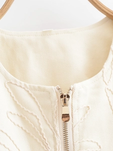 Detail of golden metal zipper and elegant floral embroidery on beige jacket neckline