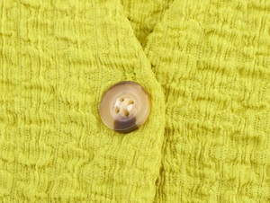 Macro shot of lime green crinkle fabric texture and tortoiseshell resin button detail