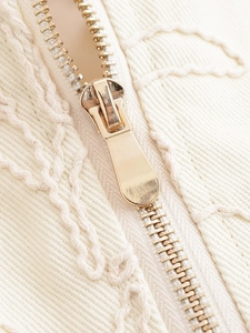 Close-up of beige jacket featuring luxury gold metal zipper and wavy rope embroidery details