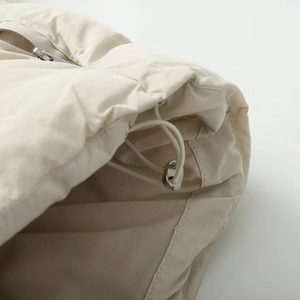 Detail of light beige quilted jacket showing metal zipper and adjustable drawstring cord