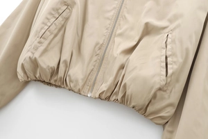 Detail of khaki bomber jacket featuring metal zipper, welt pockets, and elastic hem