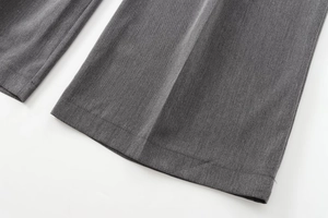 Détail du pantalon gris montrant la texture tissée et le pli marqué sur le bas