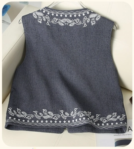 Detailed close-up of white floral embroidery on dark gray denim vest jacket