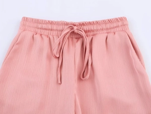 Detail of pink pleated trousers featuring an elastic drawstring waist and side pockets