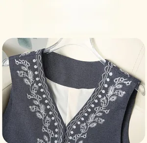 Detail of V-neck denim vest with white floral embroidery and woven fabric texture