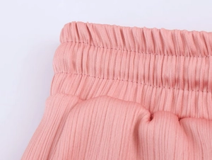 Detail shot of pink pleated suit pants featuring an elastic waistband with vertical texture