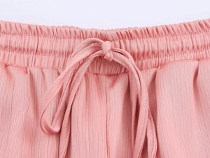 Detail of pink pleated pants featuring elastic waist and matching fabric drawstring