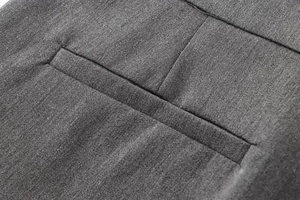 Détail macro de la poche passepoilée et des coutures sur un pantalon en sergé gris