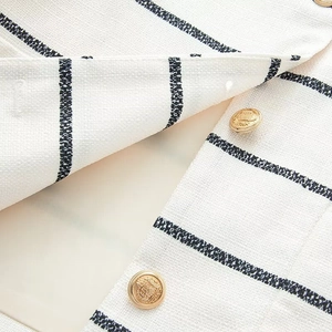 Close-up of white tweed fabric with black vertical stripes and embossed gold buttons