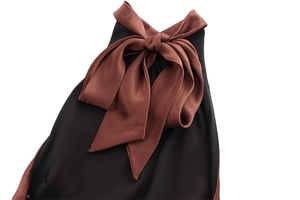 Detail of elegant black dress featuring a large brown satin bow and contrast patchwork