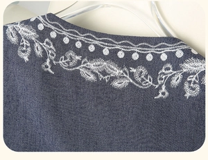 Detailed close-up of white floral embroidery on a dark blue textured denim vest