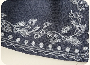 Detail of white floral embroidery and wavy stitching on dark blue denim fabric