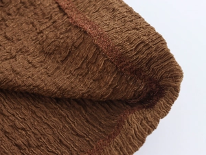 Detail shot of deep brown plissé fabric showing textured pleats and fine stitching work