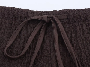 Close-up of high-waist dark brown pants with textured fabric and a neat drawstring bow