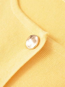 Close-up of yellow knit cardigan showing textured fabric and a gold metallic button