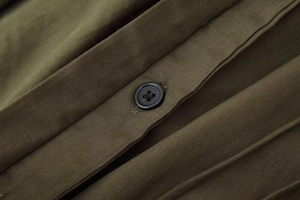 Detail of olive green fabric texture with a black four-hole button on the dress