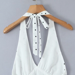 Détail d'une robe blanche dos nu avec des liens à pois noirs sur un cintre en bois