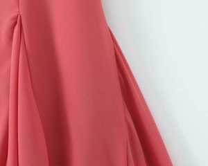 Detail of coral pink pleated chiffon dress showing delicate fabric texture and drape