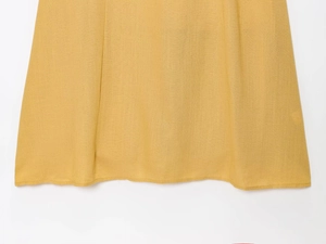 Détail de l'ourlet d'une robe jaune en lin et coton avec coutures précises et texture