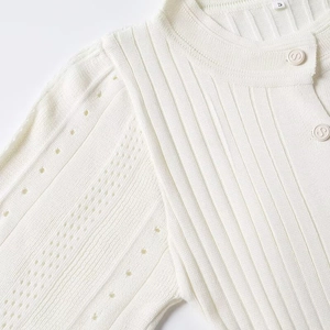 Detail of white knit dress showing pointelle sleeves and S-letter button accents