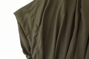 Detail view of olive green dress shoulder seams and pleated cuff fabric texture