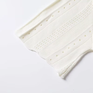 Detail of white knit dress showing vertical texture, eyelet holes and scalloped hem