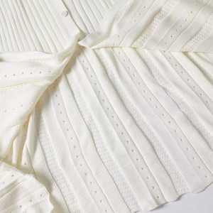 Detailed macro view of white pointelle knit dress featuring vertical ribs and white button