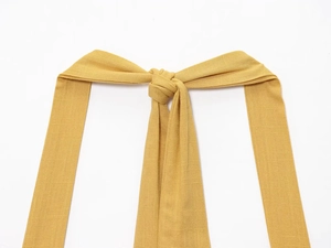 Vue rapprochée des nœuds en tissu jaune gingembre et de la texture lin de la robe