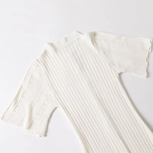Detail of white knit dress showing fine ribbed texture and hollowed-out lace on cuffs