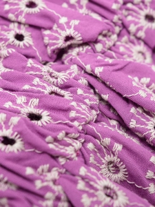 Nahaufnahme von lila Stoff mit weißer Blumen-Lochstickerei und filigranen Hohlraum-Details
