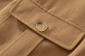Detail of a brown twill jacket pocket with a polished tortoiseshell button and neat stitching