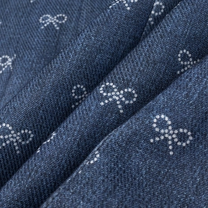 Detailed view of dark blue denim fabric with white bow patterns and twill texture