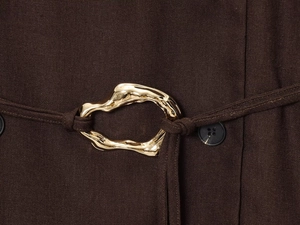 Detail of a gold metallic buckle and black button on dark brown tailored suit jacket