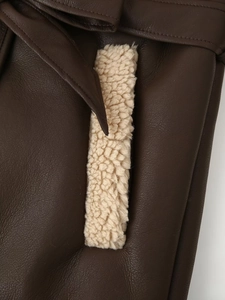 Detail of dark brown leather jacket with soft beige faux shearling lining and waist tie