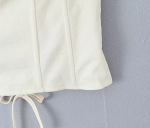 Detail of white corset top featuring boning structure and hanging decorative ties