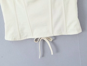 Macro detail of white corset top with boning structure and small bow accent at bottom