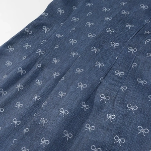 Close-up of denim dress fabric featuring white bow patterns and twill texture details