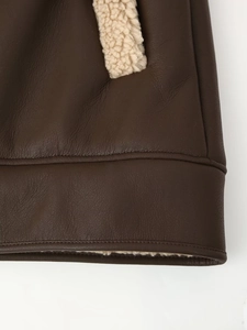 Detail of dark brown leather texture and white faux shearling trim on a coat hemline