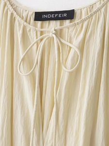 Detail of drawstring neckline on cream pleated dress showing the Indefeir brand label