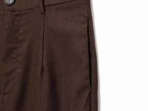 Detail of dark brown trousers waist featuring black button and pleated texture detail